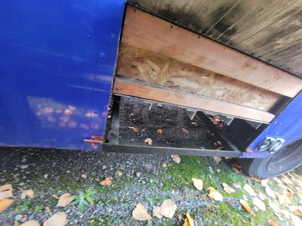 Blue 2003 Chevrolet P24 Workhorse food truck, partial view showing undercarriage with plywood paneling and open section.