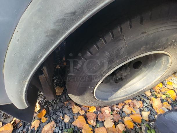 Close-up of tire and wheel of a 1973 International Step Van on gravel with fallen leaves. Visible wear and dirt.