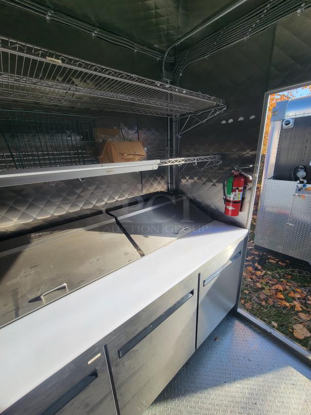 2021 24' Quality Trailer, fully equipped electric kitchen with stainless steel appliances, shelves, and fire extinguisher.