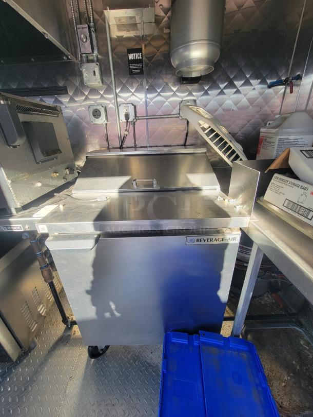 High-end 2021 16' food trailer interior with stainless steel appliances, diamond plate flooring, and Beverage-Air fridge.