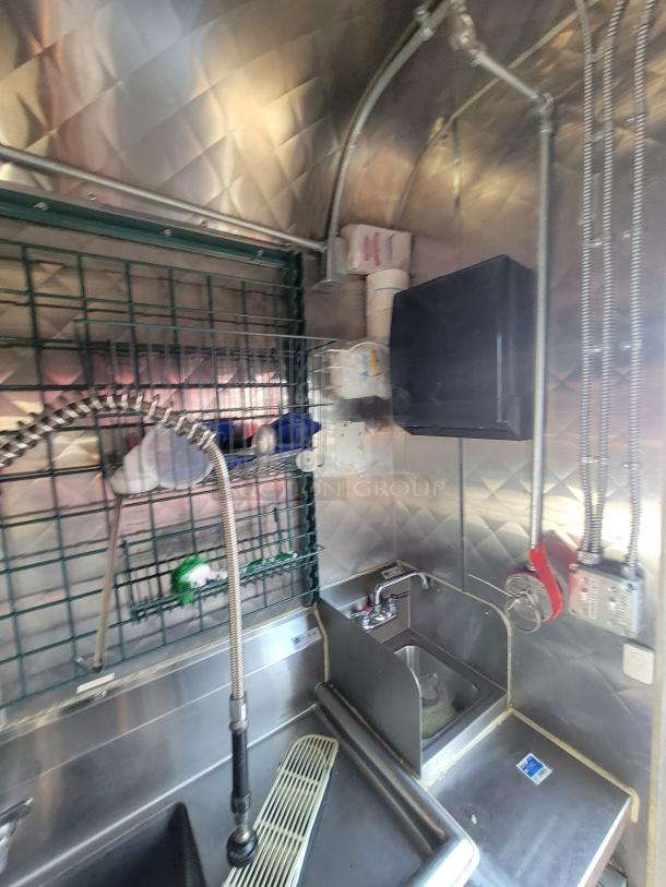 Interior of high-end 2021 commercial food trailer, featuring stainless steel sink, storage rack, and faucet setup.
