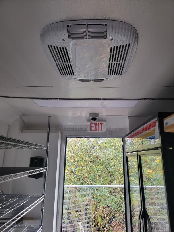 Interior view of 2021 SDG 8.5' x 20' concession trailer, showing ceiling vent, metal shelves, and an exit sign above the door.