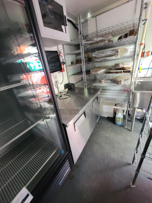 2021 Diamond Cargo 24' mobile kitchen trailer interior with stainless steel prep counters, shelves, sink, and True refrigeration unit.