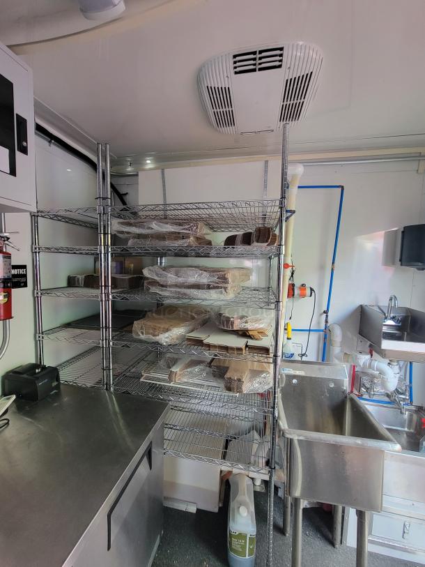 2021 24' Diamond Cargo mobile kitchen interior with stainless steel sink, wire shelving, and prep counter, ready for use.