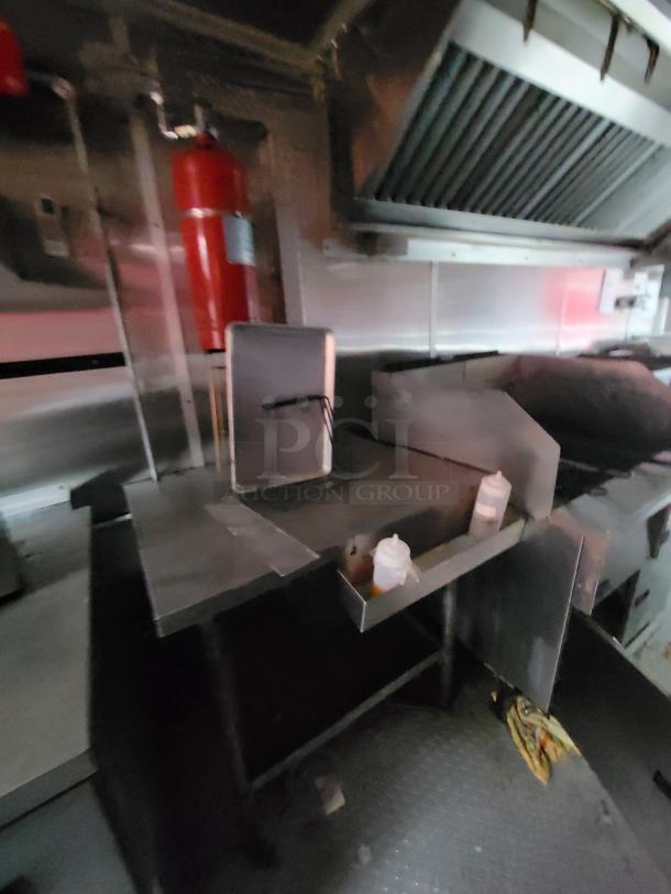 Interior of 2019 Rock Solid Cargo 24' food trailer featuring stainless steel countertops, a fire suppression system, and exhaust hood.