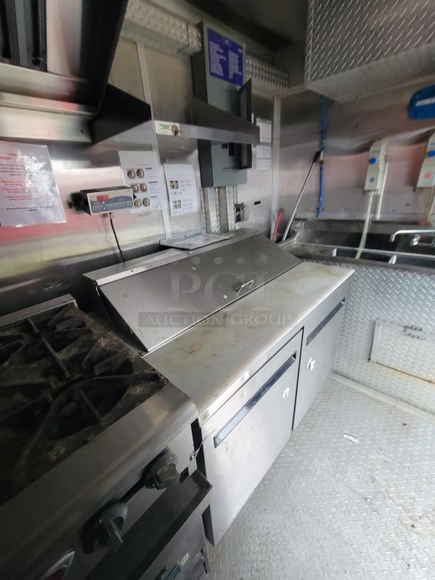 2019 24' Rock Solid commercial food trailer interior with gas range, stainless-steel prep area, and sinks. Visible signage and controls.