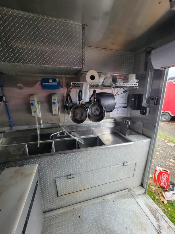 2019 24' Rock Solid food trailer interior, featuring a commercial kitchen sink, hanging pans, and stainless steel fixtures.