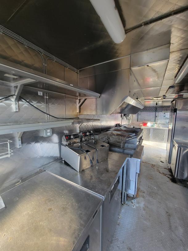 2020 Quality 24' food trailer interior with stainless steel counters, fryers, and fire suppression. Fully equipped mobile kitchen.