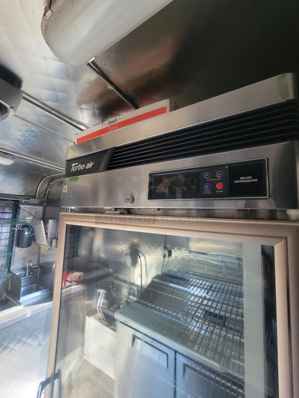 24' Quality food trailer interior with Turbo Air refrigerator, stainless steel counters, plumbing, and commercial equipment.