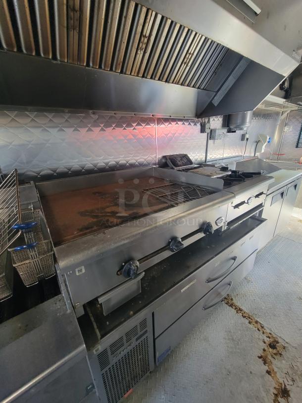 Mobile commercial kitchen trailer interior with stainless steel appliances, including grill and fryer. Equipped for high-volume use, excellent condition.
