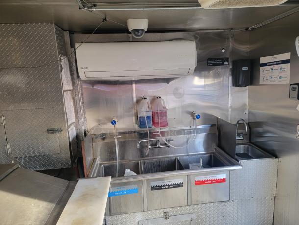 Interior of a 2019 Quality 24' food concession trailer with a commercial-grade sink setup, fire suppression system, and stainless steel surfaces.