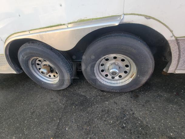 Tandem wheels of a 2019 Quality 24' food concession trailer, showing durable tires and metallic rims, on a gravel surface.