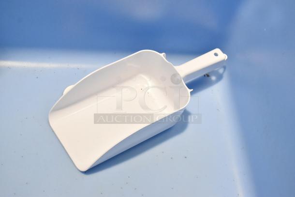 White plastic scoop, likely a component of an Ice-O-Matic ice bin, placed on a light blue surface.