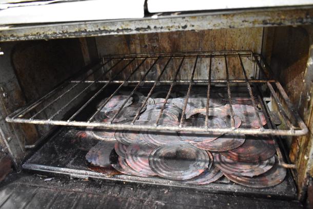 Garland SunFire commercial gas range oven interior showing signs of heavy use with discolored metal drip pans inside.