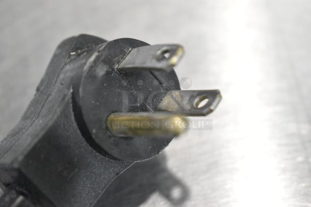 A close-up of a three-prong electrical plug, highlighting its metal prongs and black plastic casing.