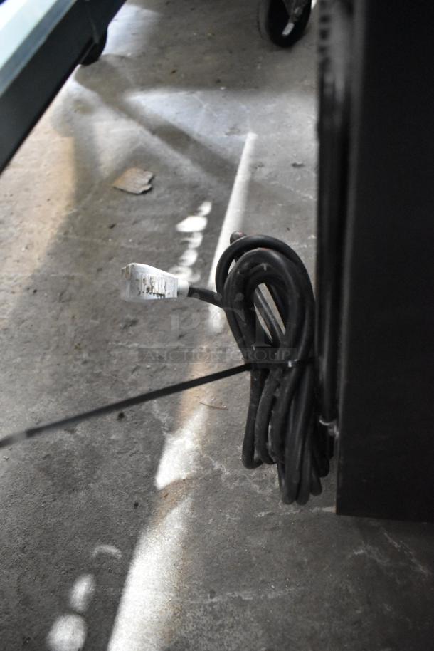 Coiled power cord of 2020 True GDM-41SL-60-HC-LD reach-in cooler, showing plug and surrounding area.
