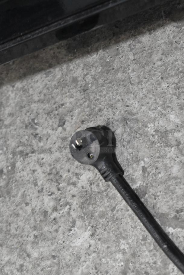 2022 True T-19F-HC freezer power plug, black, 115 volts, 1 phase, against a gray surface.