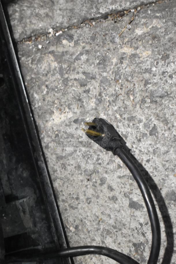 True Metal Commercial Cooler power cord on textured floor. Black plug with three prongs, 115 volts, 1 phase.