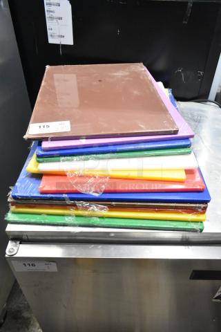 Stack of 12 color-coded cutting boards, brand new with minor scratches, various colors, wrapped in plastic, labeled as lot 115.