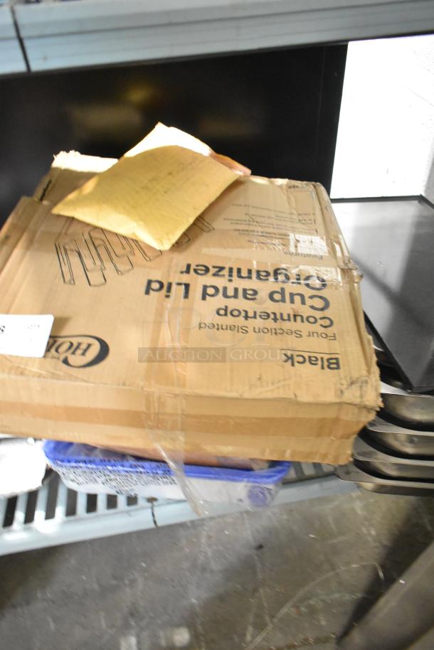 Box labeled "cup and lid organizer" with packaging materials on top, part of a tier lot including drop-in bin lids.