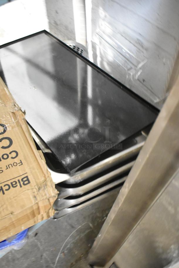 Tiered lot with a black cup and lid organizer, drop-in bin lids, and a cardboard box. Items appear in fair condition.