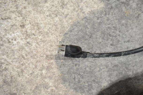 Power plug for Presto PM-20 mixer. Black, three-prong plug connected to cord, laying on textured surface.