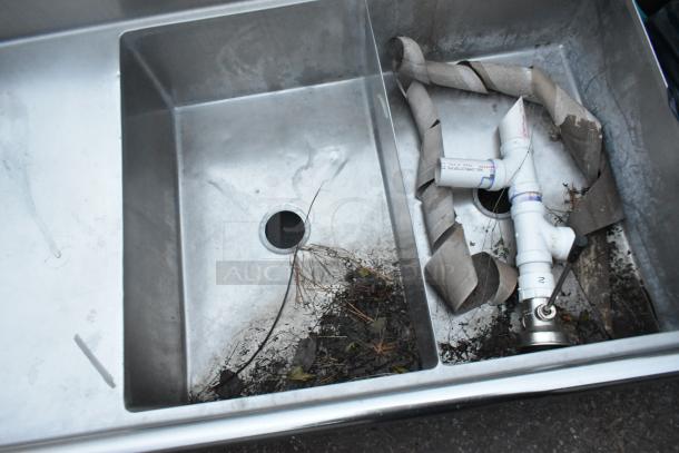 Stainless steel 3 bay sink with dual drain boards, visible wear, debris, and no legs, suitable for commercial use.
