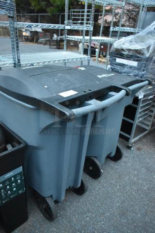 Two large gray poly trash cans with lids and wheels.