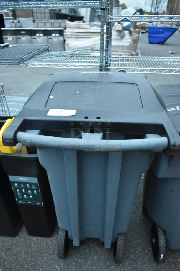 Gray poly trash can with wheels and a handle, labeled "187" on top. Rugged design for outdoor use. Sale includes two cans.