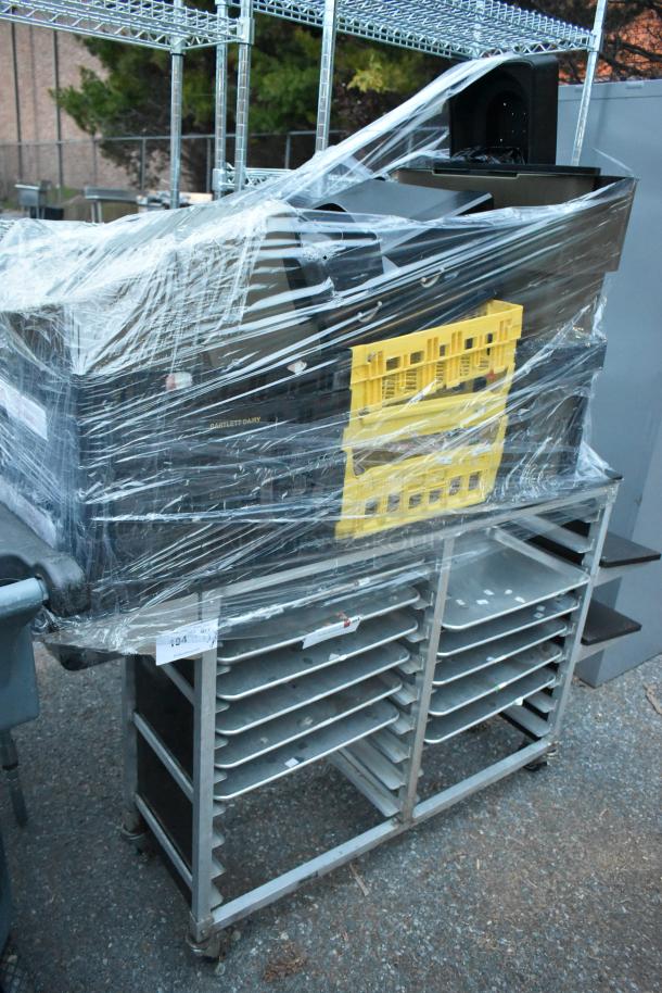 Metal commercial double pan transport rack with casters, wrapped in plastic, includes assorted contents.