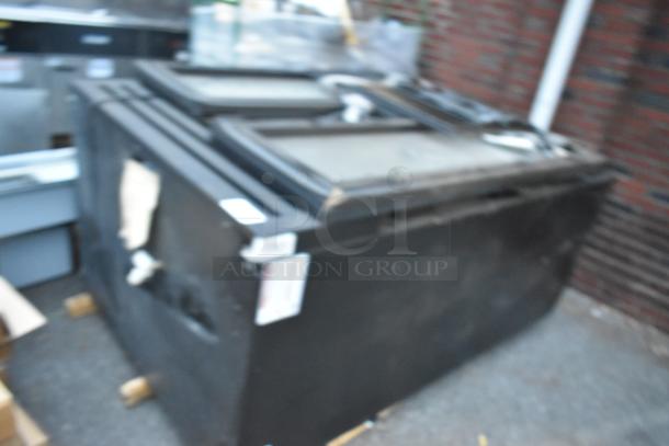 Metal commercial 2-door reach-in cooler, black exterior, some visible wear. Labels attached; details not readable.