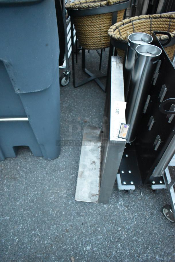 Stainless steel tabletop, rectangular, in fair condition with visible rust on edges, resting against metal framework.