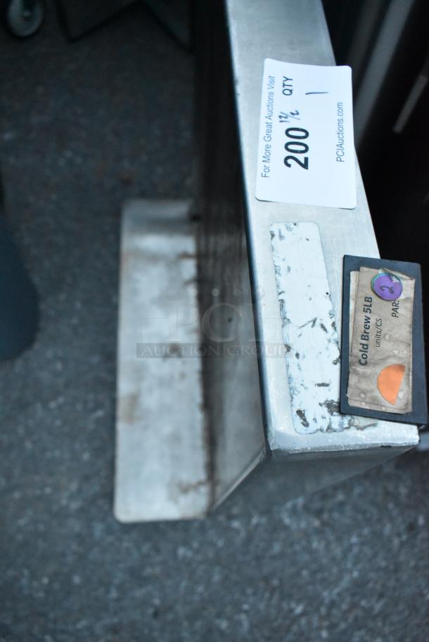 Stainless steel tabletop with visible wear, auction tag reading "200 1/2 QTY," and label marked "Cold Brew 5LB."