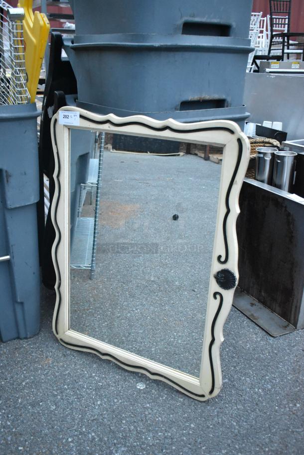 Vintage mirror with wavy carved wooden frame and black accents, set outdoors. Minor wear visible; tag "202 QTY 1".