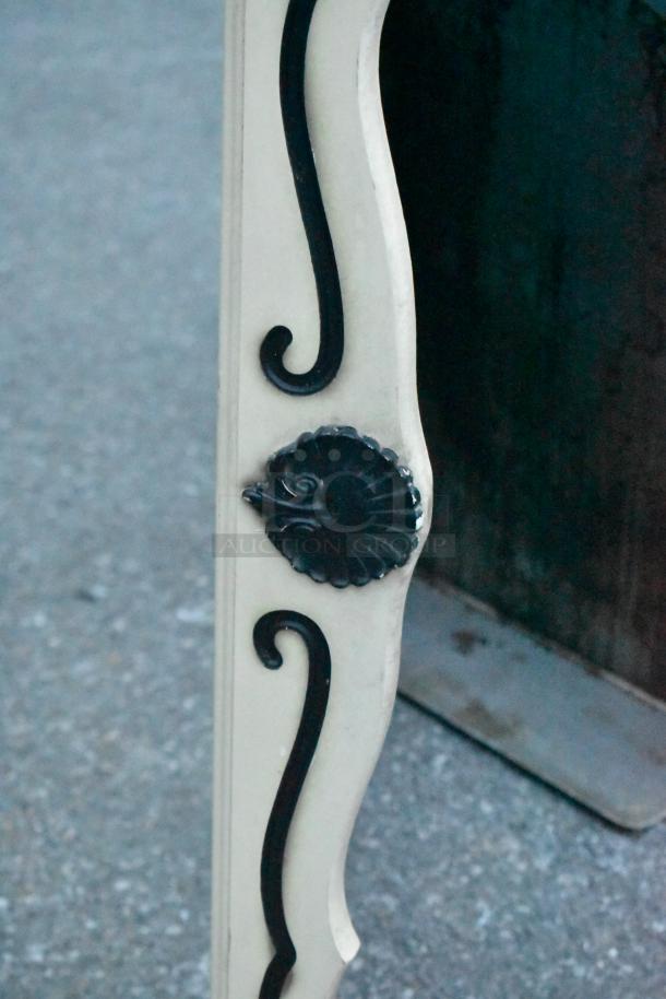 Decorative mirror frame with ivory background and black scroll detailing, featuring a central black shell motif.