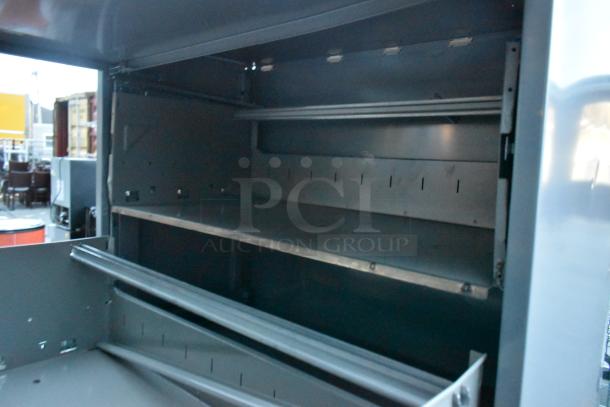 Gray metal filing cabinet with four drawers and one door, interior view showing shelving. Minimal wear. Ideal for office use.