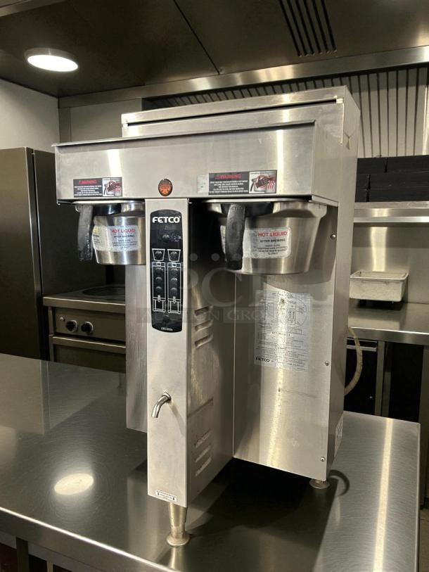 Fetco CBS-2052e twin coffee brewer in great condition on stainless steel counter. Dual dispensers, Fetco branding visible.