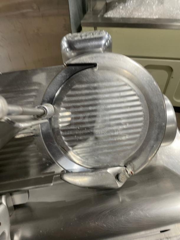 Stainless steel commercial deli meat slicer on countertop, featuring a large rotary blade and sturdy grip handle.