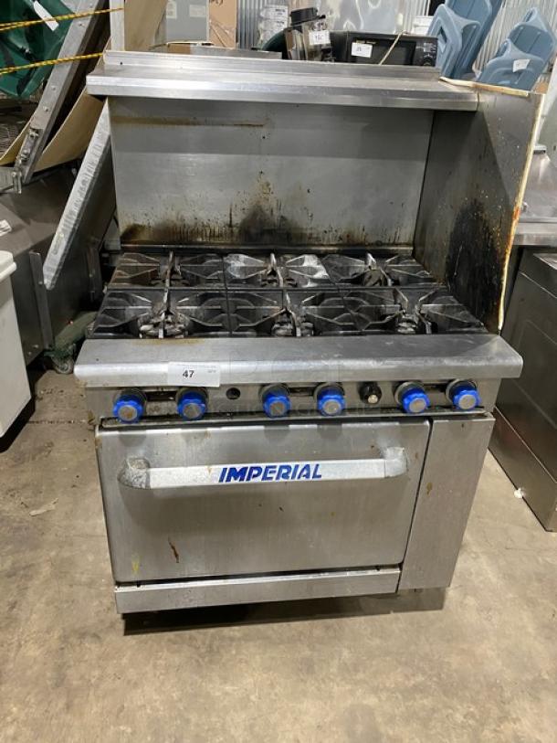 Stainless steel Imperial 6-burner gas stove with overhead salamander shelf and full-size oven. Used condition, visible wear.