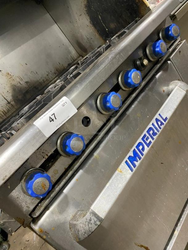 Imperial stainless steel 6 burner gas stove with overhead salamander shelf and full-size oven. Features blue knobs. Model tag visible.