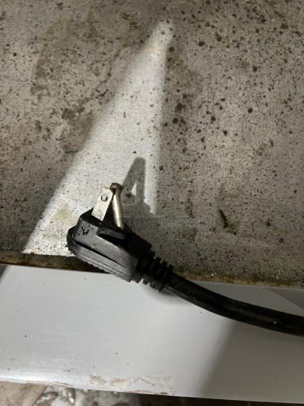 Black power cord with a three-prong plug, resting on a speckled concrete surface.