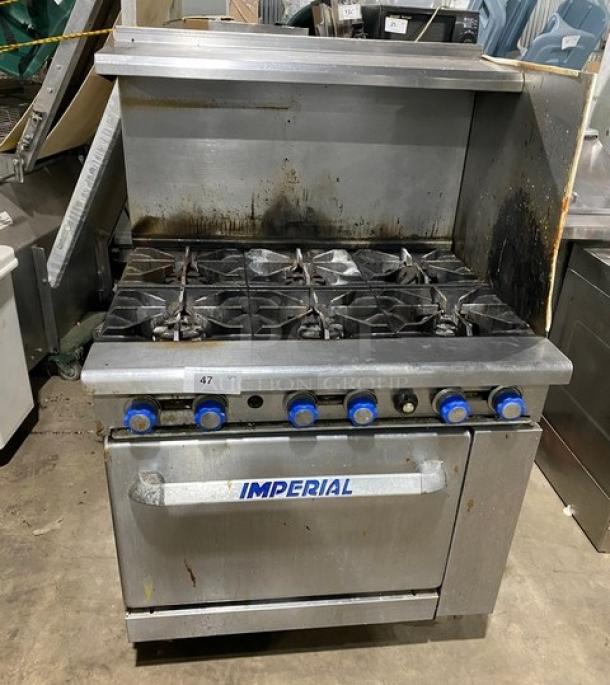 Stainless steel Imperial 6-burner gas stove with overhead salamander shelf and full-size oven. Used condition, visible wear.
