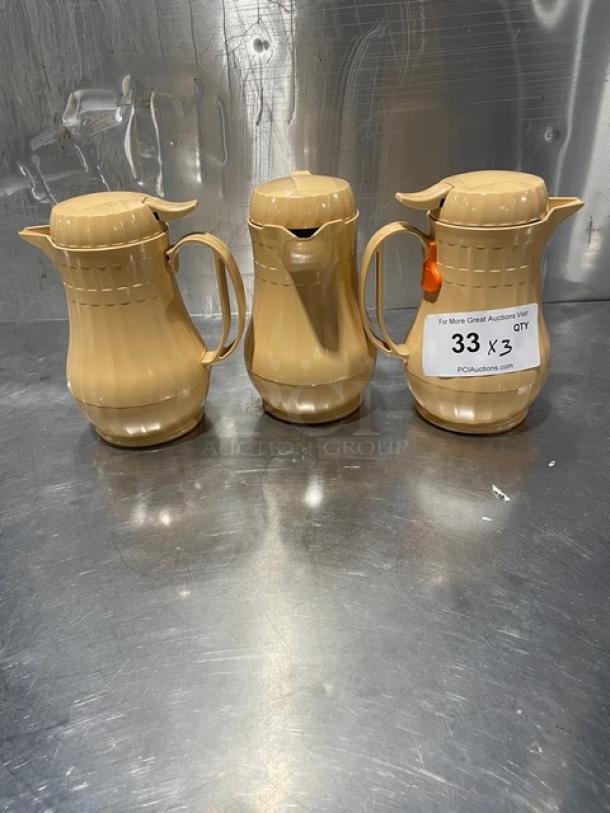 Set of 3 new Service Ideas insulated ABS plastic coffee carafes with push button lids, beige color, lot number tag visible.