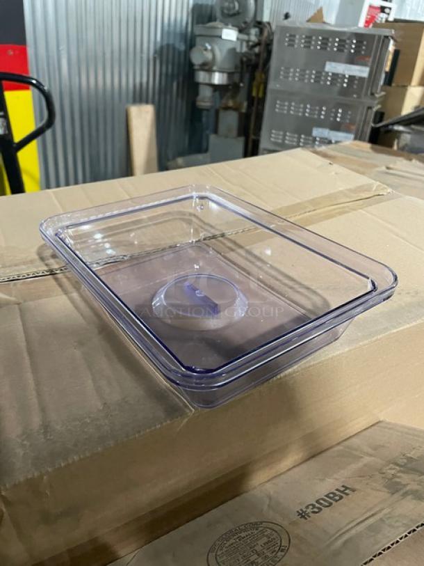 Clear rectangular plastic container with lid placed on cardboard box, in warehouse setting.