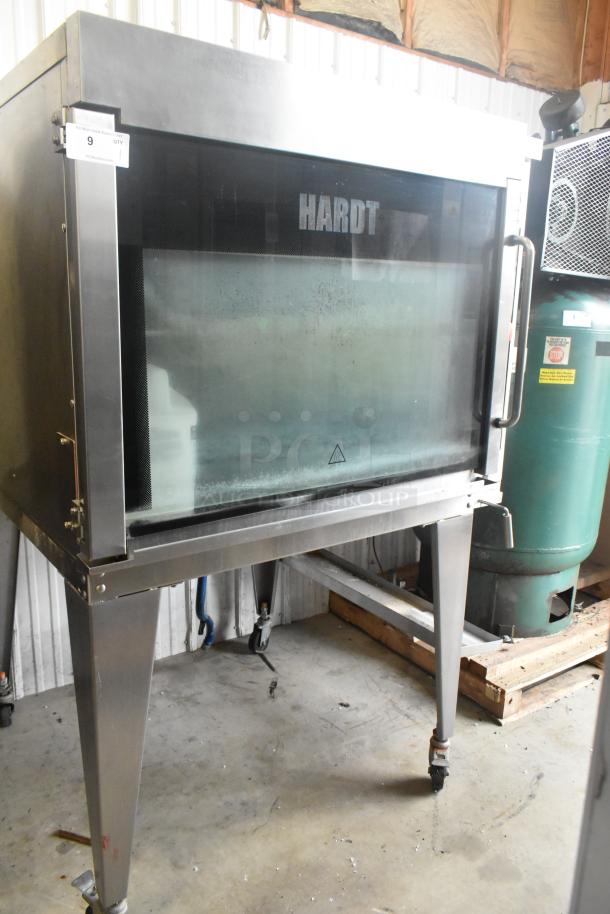 Hardt Inferno 4500 stainless steel commercial rotisserie oven with skewers, metal legs, and casters. Natural gas powered.
