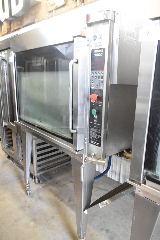 Hardt Inferno 4500 stainless steel rotisserie oven, natural gas, with skewers, metal legs on casters, control panel visible.