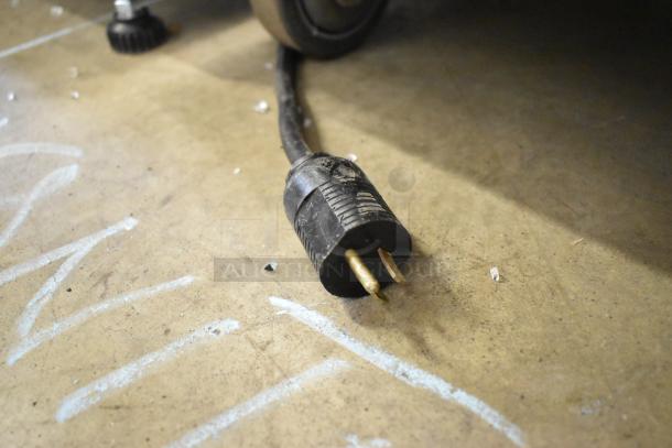 A heavy-duty commercial plug attached to the JBT 2ND-GEN-MFJ-HE citrus juicer's power cord on a concrete floor.