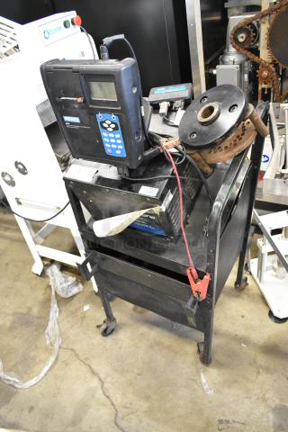 Midtronics GRB diagnostic station on cart, featuring a digital display and control panel. Shows wear, with clamp cables attached.