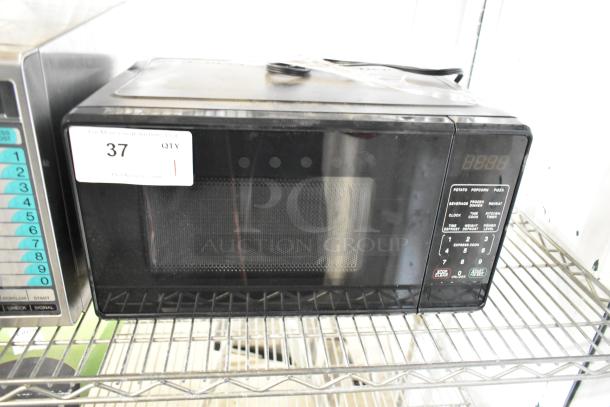 Brand new 2024 Mainstays MS8436127995-01 countertop microwave, black, 120V, 1 Phase. Scratch and dent condition, auction label visible.