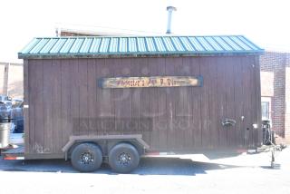 Fully outfitted food trailer with wooden exterior, green metal roof, and sign. Equipped with commercial-grade kitchen appliances.
